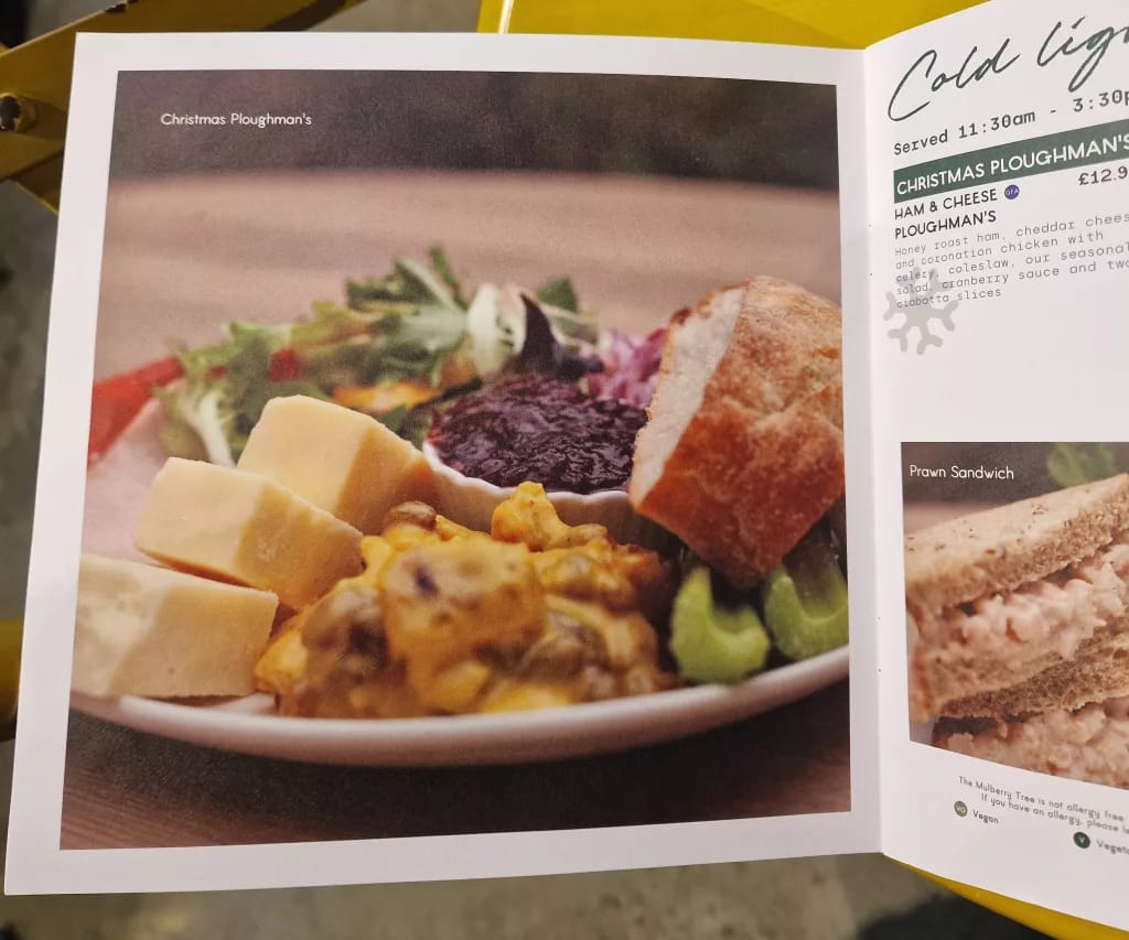 Printed menu showing a Christmas ploughman’s lunch with cheese cubes, coronation chicken, crusty bread, salad and a ramekin of chutney.