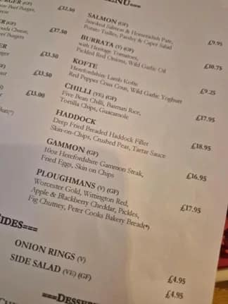 Close-up of a pub menu showing dishes including haddock, gammon, and Ploughman’s lunch with prices.